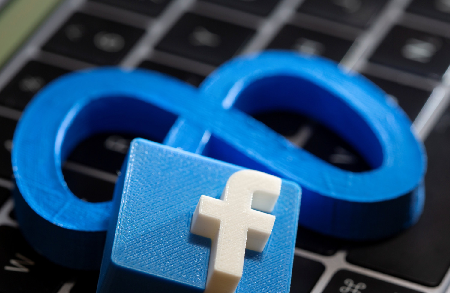 une impression 3d du nouveau logo de facebook meta et le logo de facebook sont places sur le clavier d un ordinateur portable dans cette illustration