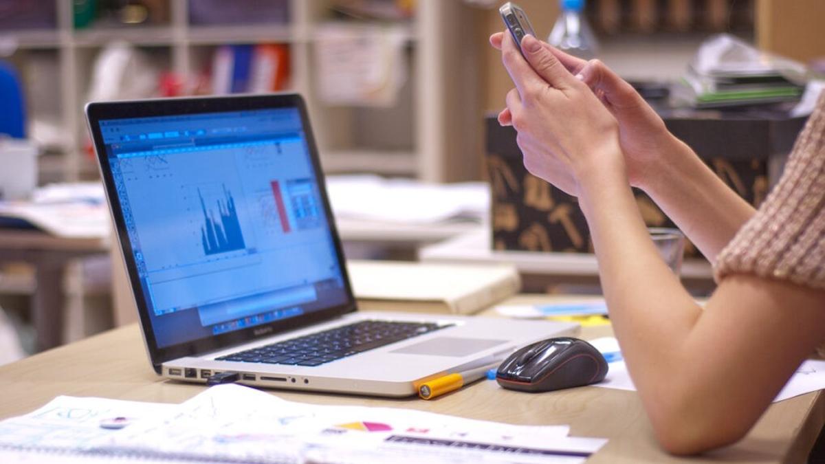 Una mujer consulta su teléfono móvil para realizar una trasferencia bancaria.