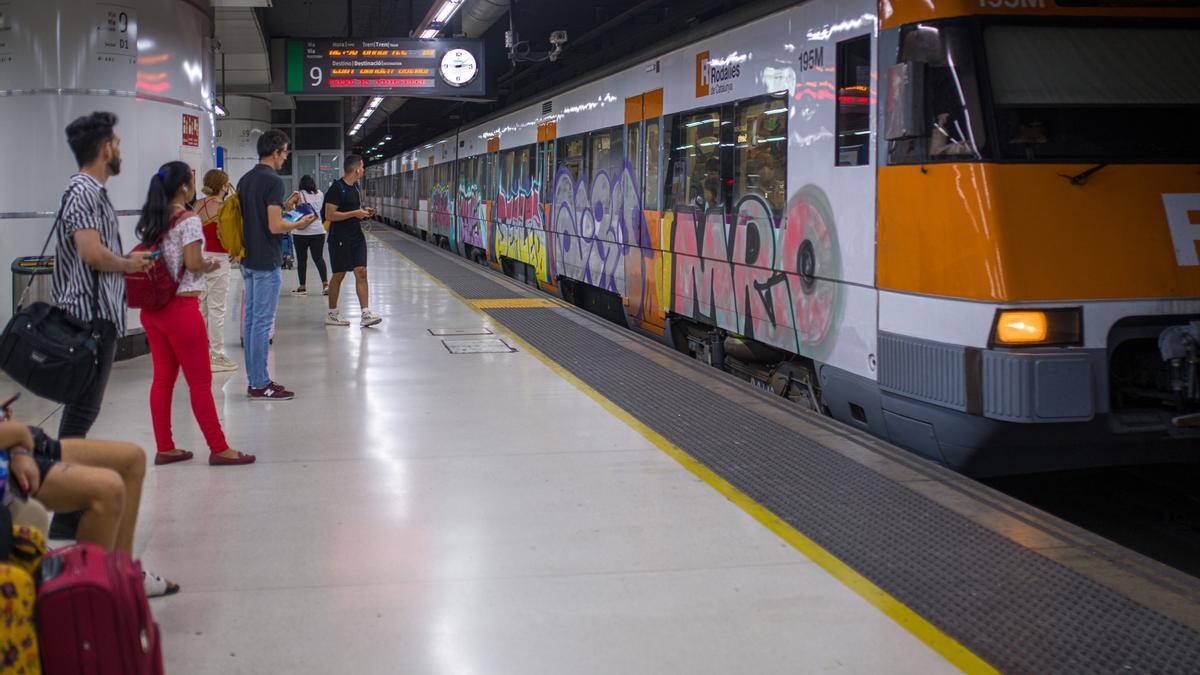Archivo - Viajeros esperan la llegada de un tren en uno de los andenes de la estación de Sants
