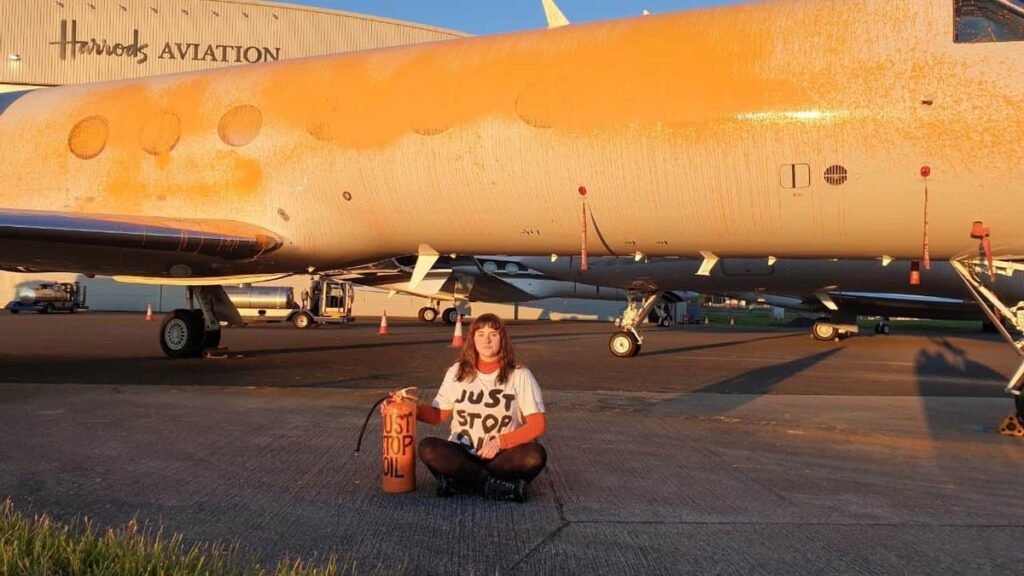 Una activista de Just Stop Oil se sienta en señal de protesta frente a jet privado que acaba de rociar de pintura.